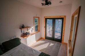 Un dormitorio con cama, ventana, puerta, ventilador de techo y vista a una terraza.