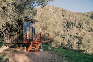 A cabin with a wooden staircase and a small platform, surrounded by a forested hillside.