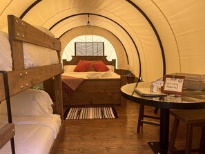 Una habitación con tienda de campaña, una cama, una mesita y un cartel de bienvenida.