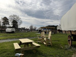 Un montaje para picnic con una mesa y sillas, un carro cubierto y un carruaje descubierto en un campo cubierto de hierba.