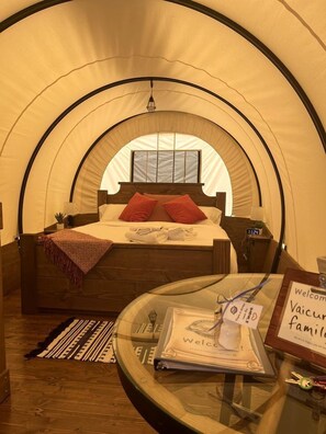 Una habitación con tienda de campaña, una cama, una mesa de vidrio con un letrero de bienvenida y un reloj.