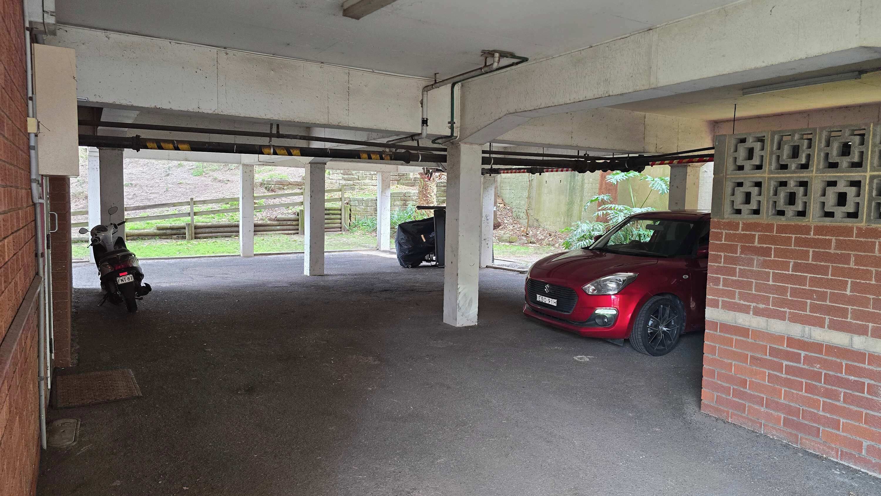 A covered parking area with a red car and a motorcycle.