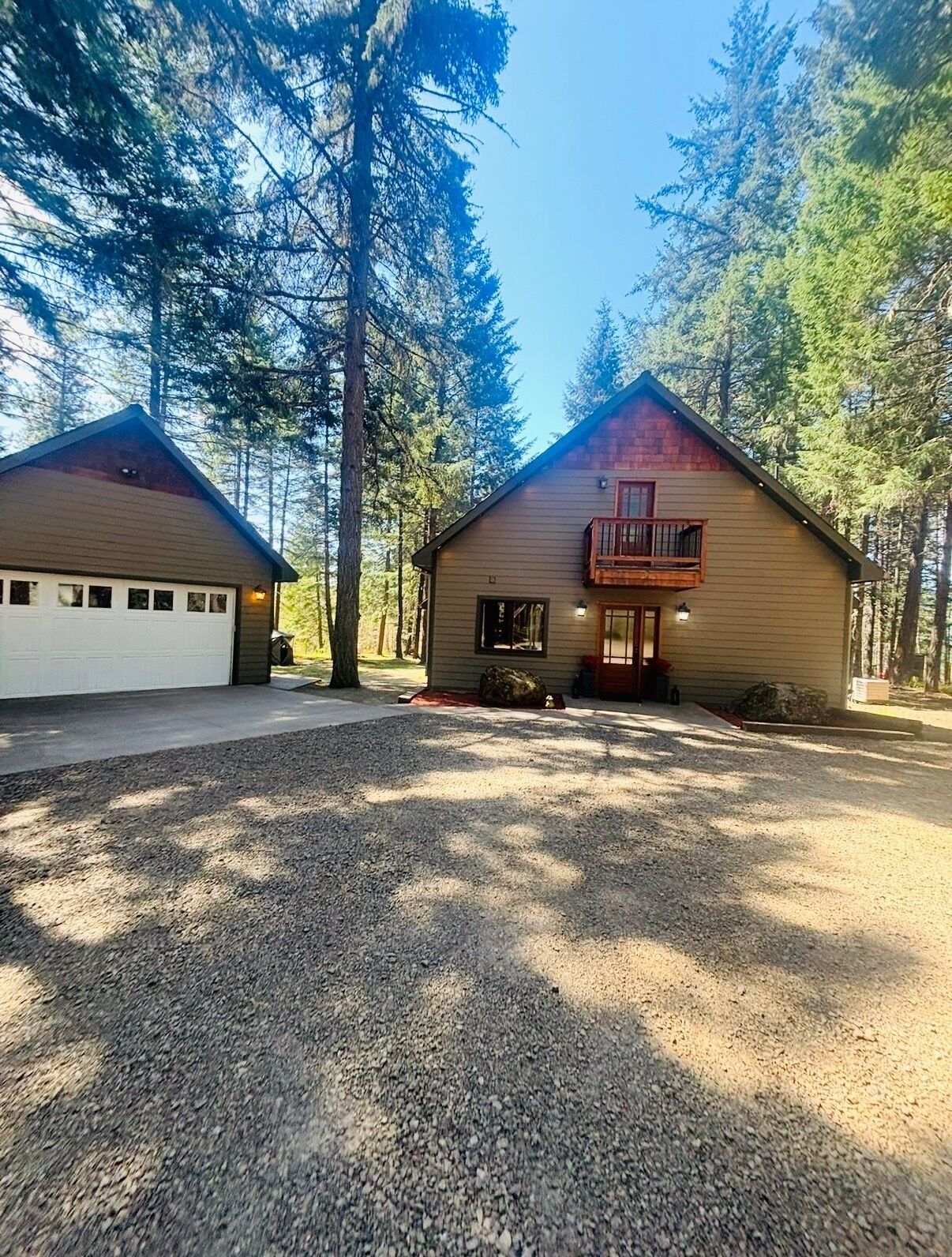 A cabin with a garage, a porch with a bench, and a large window.