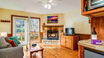 A cozy living room with a stone fireplace, wooden furniture, a television, and a wine bottle on a counter.