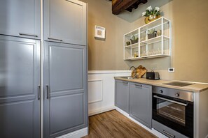 A kitchen with grey cabinets, a wooden countertop, a built-in oven, and a white shelf with glassware. - Santa Croce Cozy Studio (Firenze)