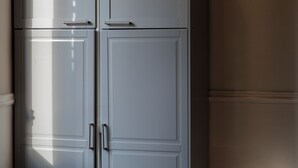 Een kast met twee deuren en een handgreep, geplaatst tegen een wand met een houten vloer.