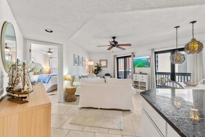 Ein modernes Wohnzimmer mit einem weißen Sofa, einem Essbereich mit weißem Tisch, einer Küche mit schwarzem Arbeitsplatz und einem Balkon mit Blick.