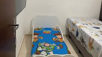 Quarto com uma cama de solteiro, janela com persianas, televisão na parede e uma porta.