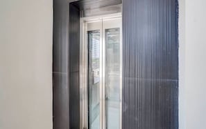A modern elevator with glass doors and a metallic frame. - Hotel Arya Luxury  (Varanasi)