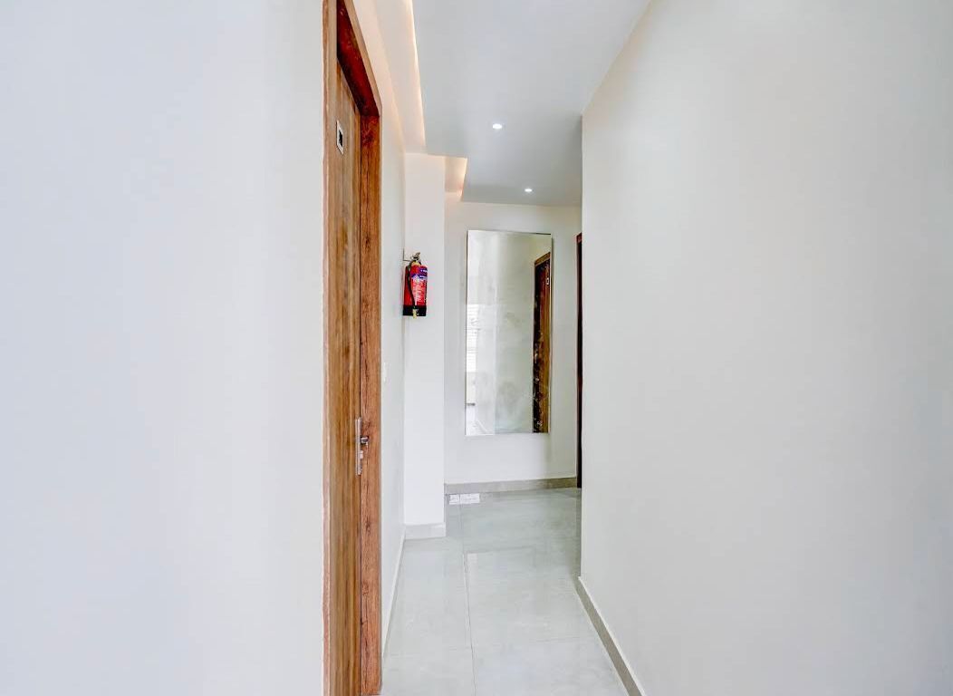 Un pasillo con una puerta de madera, un extintor y un espejo en la pared.