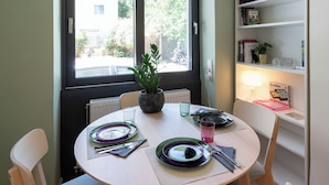 Et spiseområde med et rundt bord, stole, en potteplante og et bogreol med bøger og pynteting.