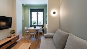 En stue med sofa, fjernsyn hængt på væggen, spisebord med stole og en potteplante.