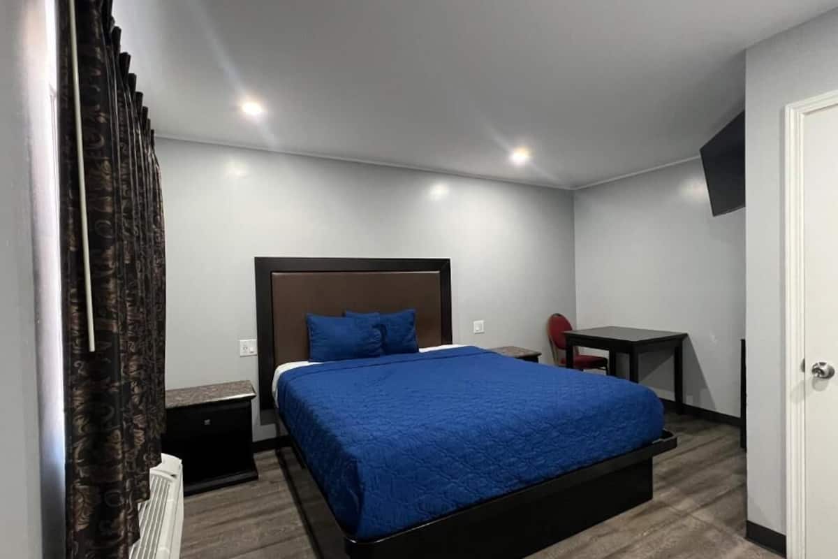 A bedroom with a bed, a desk, a chair, a radiator, and a TV on the wall.