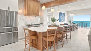 Una cocina moderna con una isla central, electrodomésticos de acero inoxidable, taburetes de bar de madera y vistas al océano.