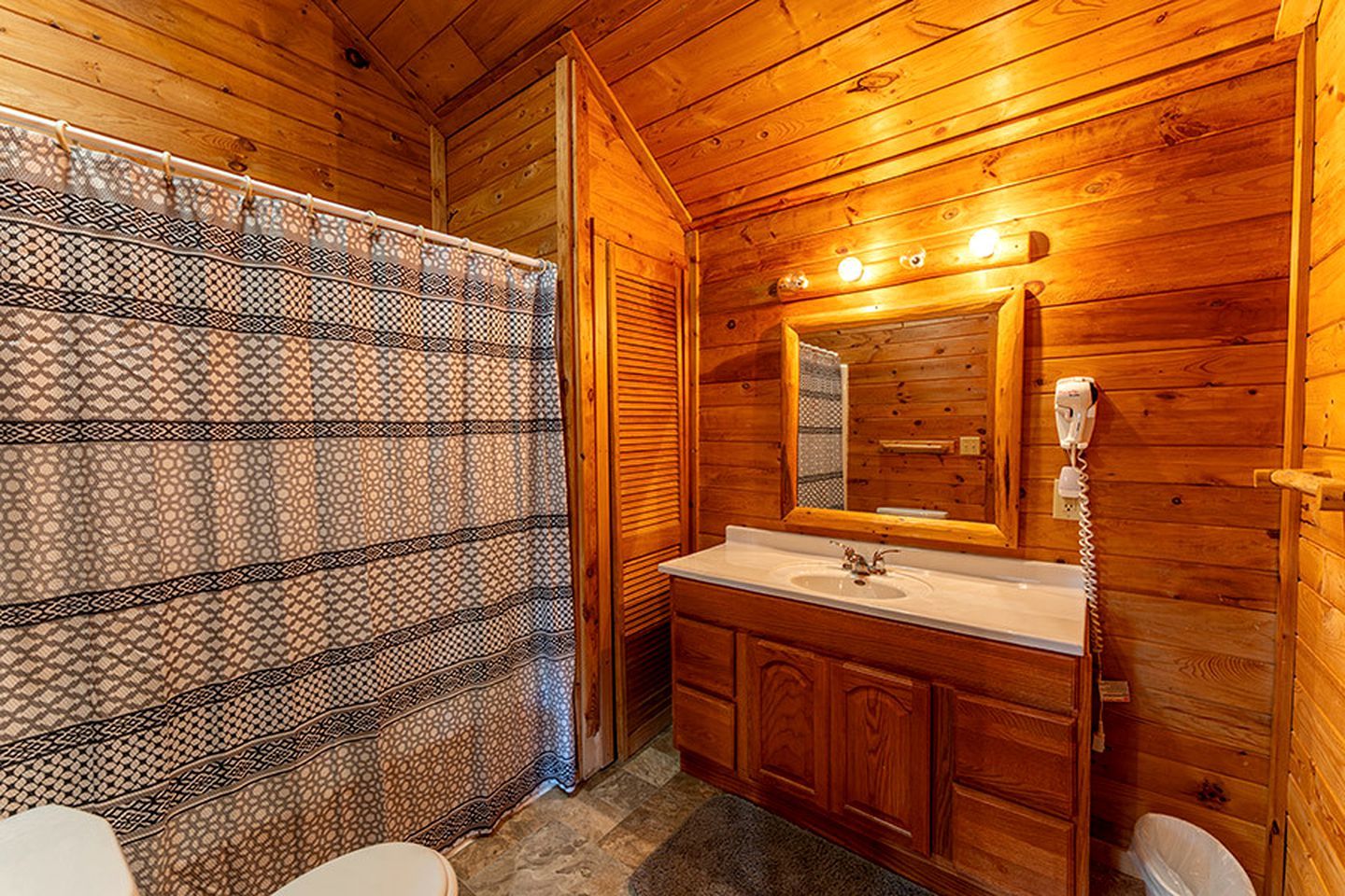 Ein Badezimmer einer Holzhütte mit einer gemusterten Duschvorhangs, einem Waschbecken mit Spiegel und einem Telefon.