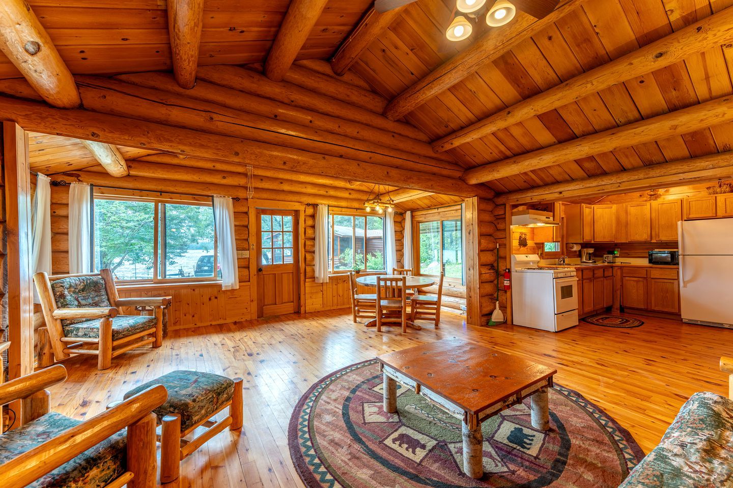 L’intérieur d’une cabane en rondins comprend un coin repas, une cuisine et de grandes fenêtres.