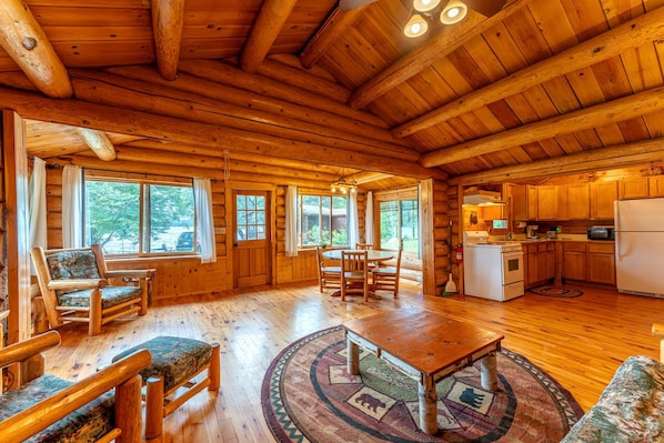 A log cabin interior with a dining area, kitchen, and large windows. - Ely Pet-Friendly Cabin Rental for Memorable Lakeside Vacations in Minnesota (Ely)