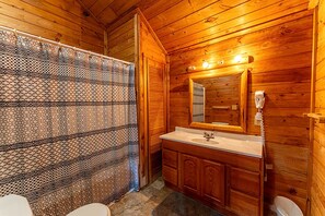 Ein Badezimmer einer Holzhütte mit einer gemusterten Duschvorhangs, einem Waschbecken mit Spiegel und einem Telefon.