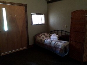 A small bedroom with a single bed, a window, a wardrobe, and a door.