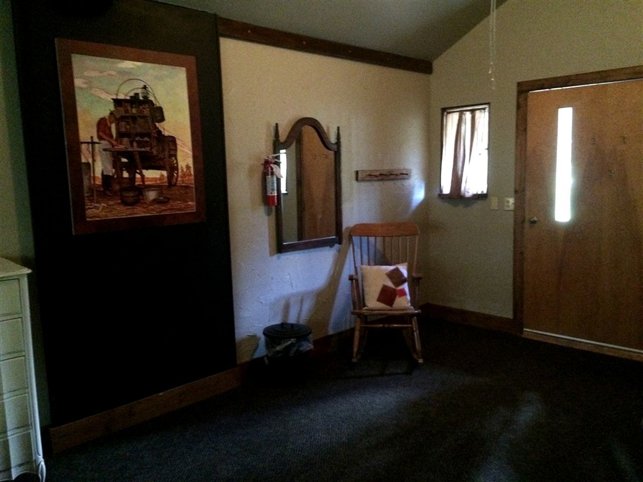 A room with a wooden door, a chair, a framed picture on the wall, and a mirror.