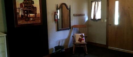 Una habitación con puerta de madera, una silla, un cuadro en la pared y un espejo.