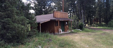 A small wooden cabin with a porch, surrounded by dense forest.