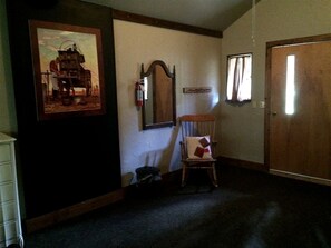 A room with a wooden door, a chair, a framed picture on the wall, and a mirror.