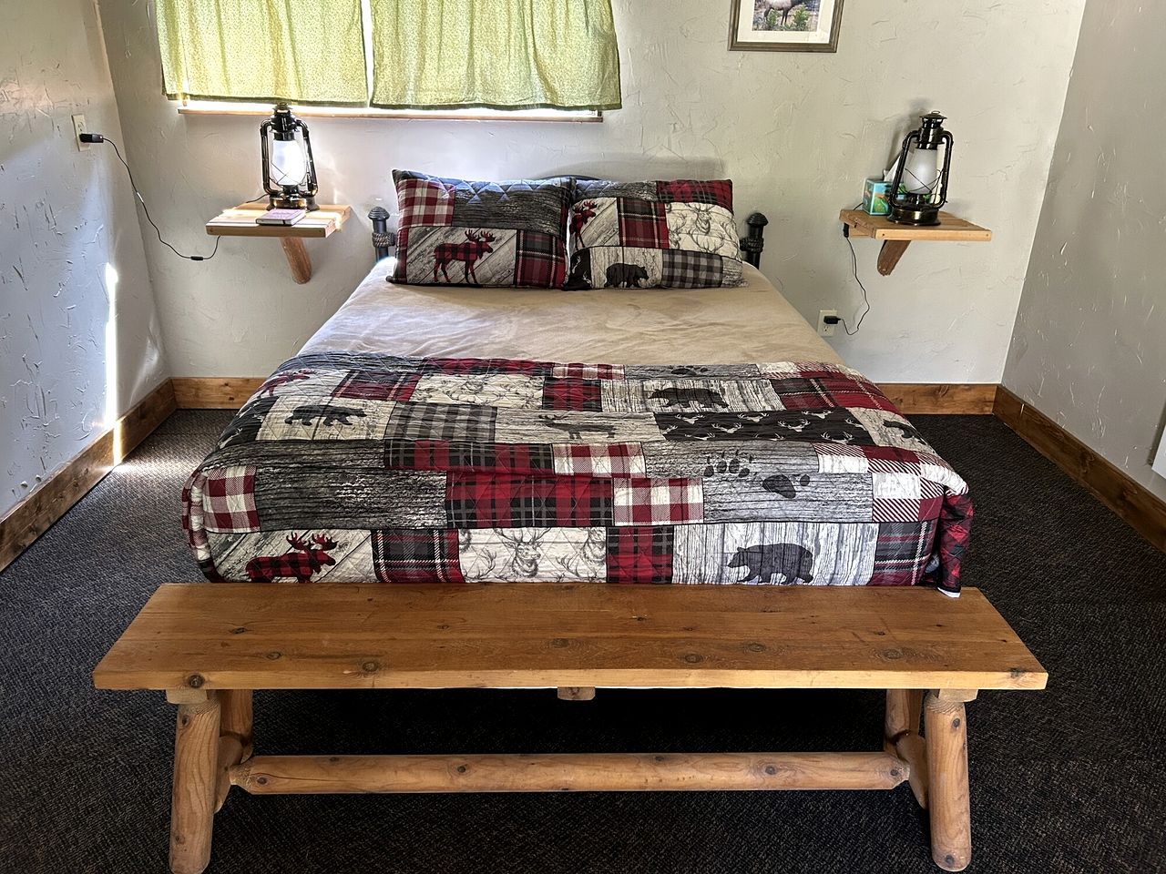 A bed with a quilted blanket, two bedside tables with lanterns, and a wooden bench in front of the bed.