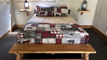 A bed with a quilted blanket, two bedside tables with lanterns, and a wooden bench in front of the bed.