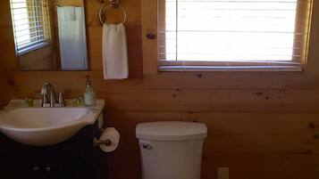 A wooden cabin bathroom with a sink, toilet, and window.
