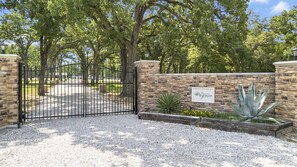 A gated entrance with a stone wall, a sign reading 'Fountain of Ragasse,' and a gravel driveway.