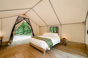 Una tienda de campaña con una cama, una ventana y vistas al bosque.