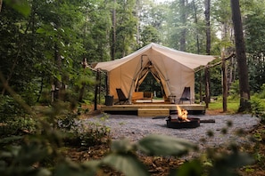 A tent with a fire pit, two chairs, and a wooden deck in a forest.
