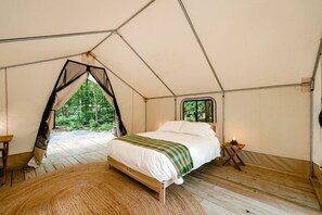 A tent with a bed, a window, and a view of the forest. - Gorgeous Safari Tent in the Lake George Area of the Adirondack Mountains, Perfect for a Family Weekend Away (Corinth)
