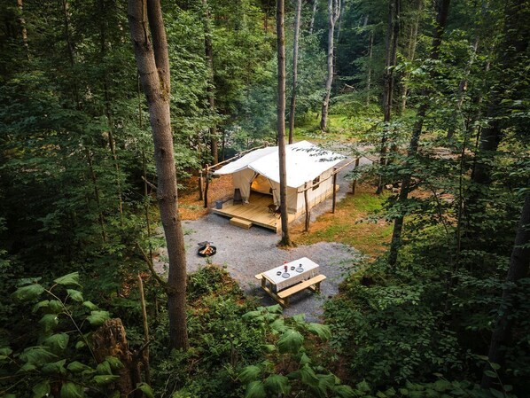 A forested campsite with a tent, a picnic table, and a fire pit.