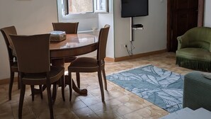 Un coin repas avec une table ronde et des chaises, un téléviseur fixé au mur, un canapé vert et un tapis à motifs.