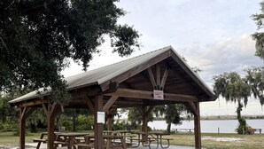 A wooden pavilion with picnic tables, a sign indicating 'Garrett & Turner,' and a view of a lake.