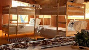 A tented accommodation with bunk beds, a central table, and a view of the outdoors.