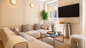 Een woonkamer met een beige bank, een salontafel, een televisie en een plant.