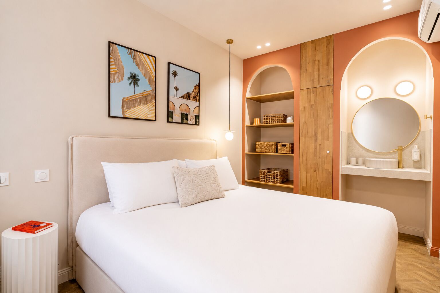 Une chambre à coucher avec un lit, une table de chevet sur laquelle se trouve un livre, une armoire avec des étagères et un miroir.