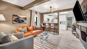 Een woonkamer met een bank, salontafel en kunstwerken. Er is een keuken met barkrukken en een eettafel. Een flatscreen-tv hangt aan de muur.