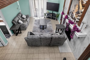 A living room with a grey sofa, a coffee table, a TV, and a fireplace with purple flowers. - Spacious Dallas Stay Near Downtown Attractions (Dallas)
