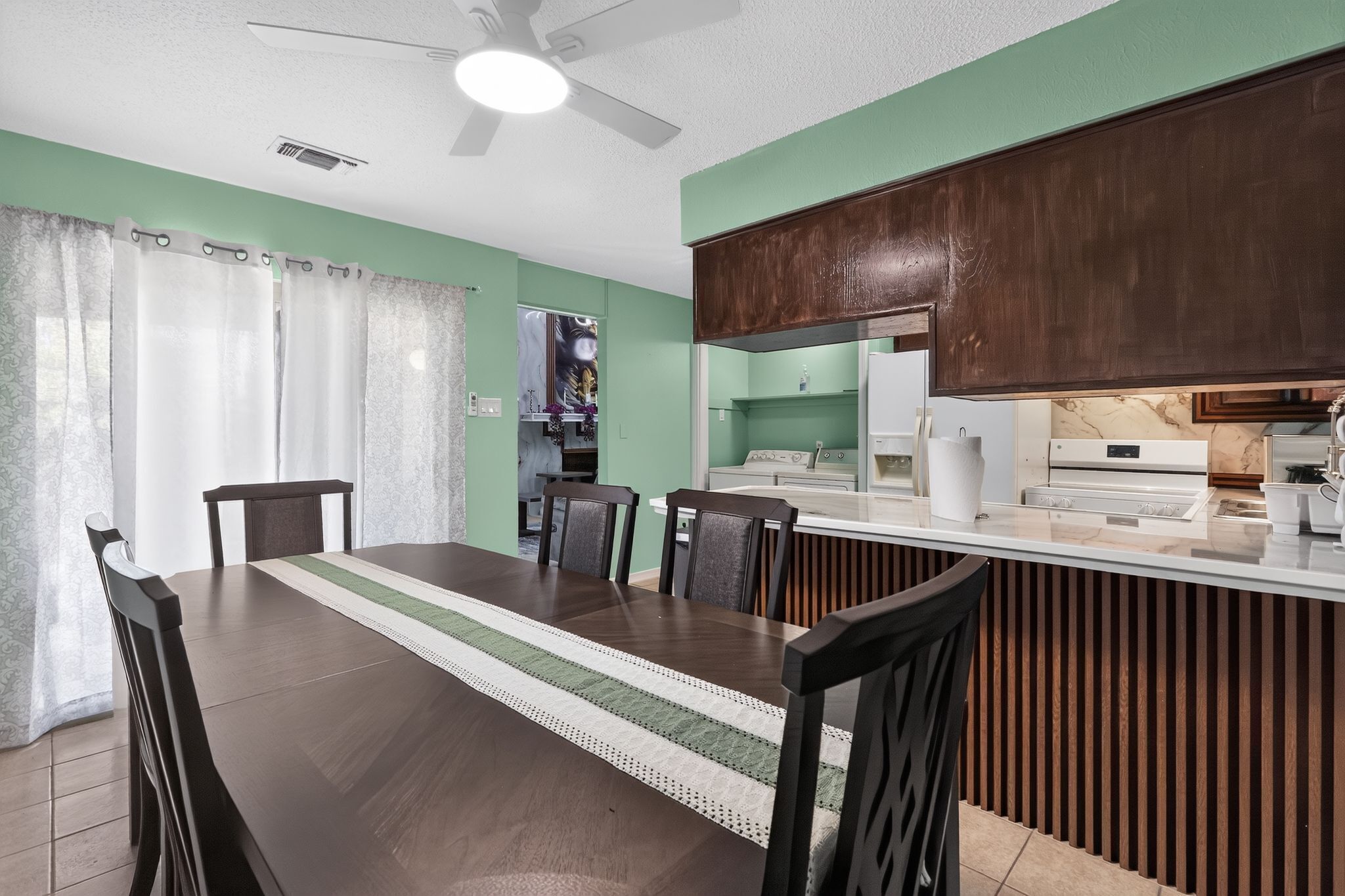 Un comedor con una mesa larga, sillas y una cocina con armarios de madera.