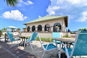 An outdoor patio with blue chairs and tables, a building with arched windows, and a clear blue sky. - Easy Breezy at Barefoot Resort w Amazing Pool (North Myrtle Beach)