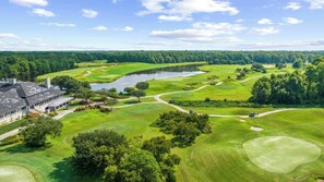 A golf course with a clubhouse, a lake, and surrounding forest. - Easy Breezy at Barefoot Resort w Amazing Pool (North Myrtle Beach)
