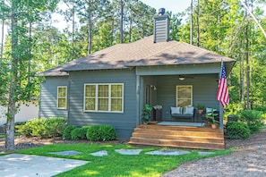 A single-story house with a porch, a chimney, and an American flag. - Modern Family-oriented 3BR 2BA Smart Home | Lake Martin Access | Near Auburn University (Tallassee)