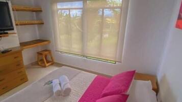 A bedroom with a wooden ceiling, a bed with white and pink bedding, a window with a view, and a wooden dresser.