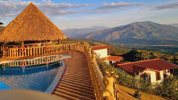 A resort with a thatched-roof structure, a pool, and a view of mountains.
