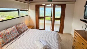 A bedroom with a bed, a wooden ceiling, a ceiling fan, a window, and a door leading to a balcony.