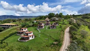 A rural setting with multiple houses, a dirt road, and a hilly landscape.